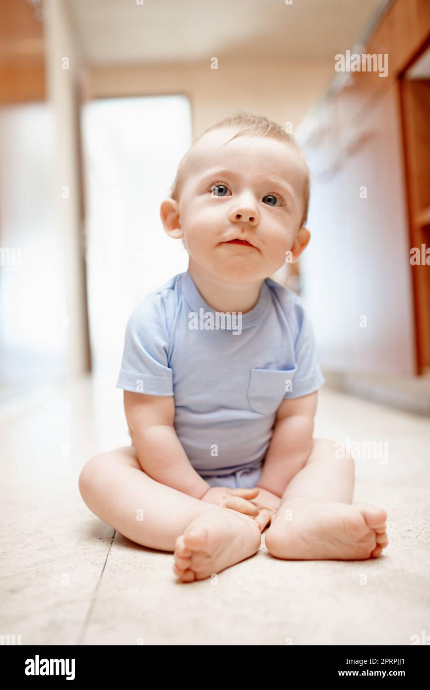 At home in the kitchen. A baby boy sitting on the kitchen floor. Stock Photo