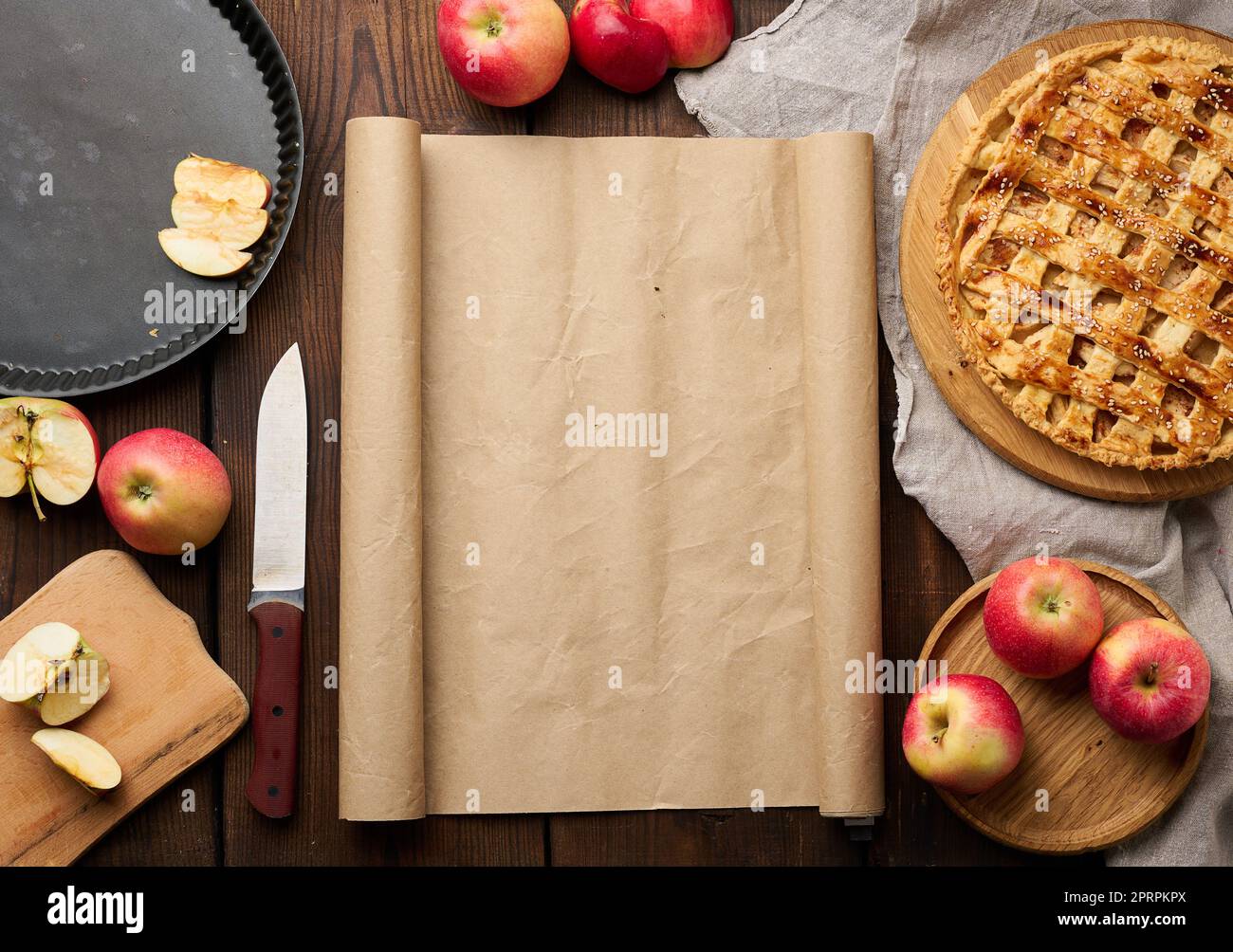 Round baked pie with apple filling on a wooden board and ingredients, brown table. Stock Photo