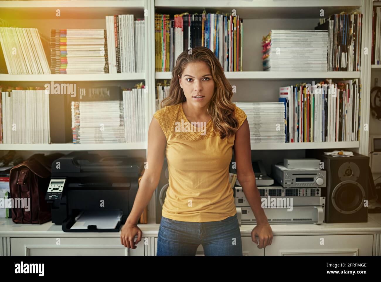 This working from home thing really suits me. Portrait of a woman standing in front of bookshelves in her home office. Stock Photo