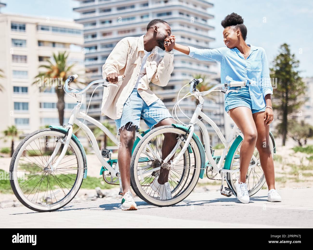 Black man, kiss woman hand and outdoor park holiday in miami. Couple on romantic summer date, cycling in city street and happy girlfriend. Young boyfriend in love, leisure bike ride and sunshine Stock Photo