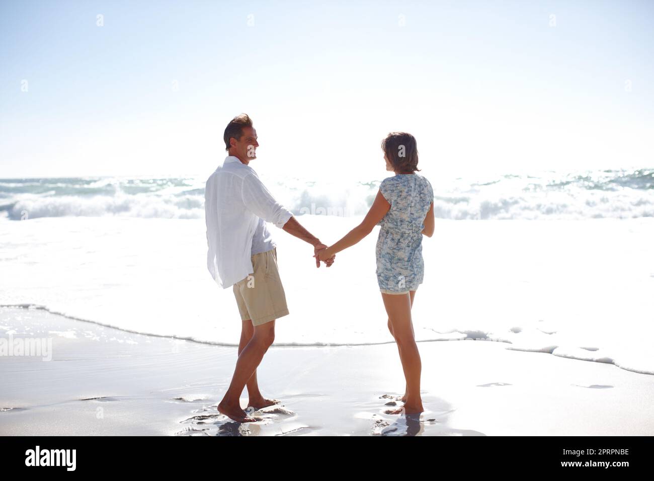 Enjoying the romance of the ocean. Rearview of a happy mature couple walking hand in hand on the beach. Stock Photo