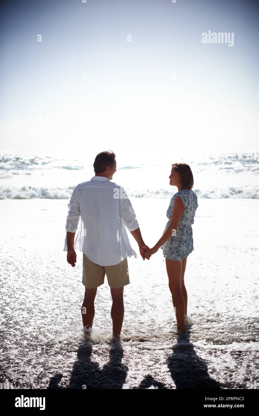 With summer comes the romance. Rearview of a happy mature couple walking hand in hand on the beach. Stock Photo