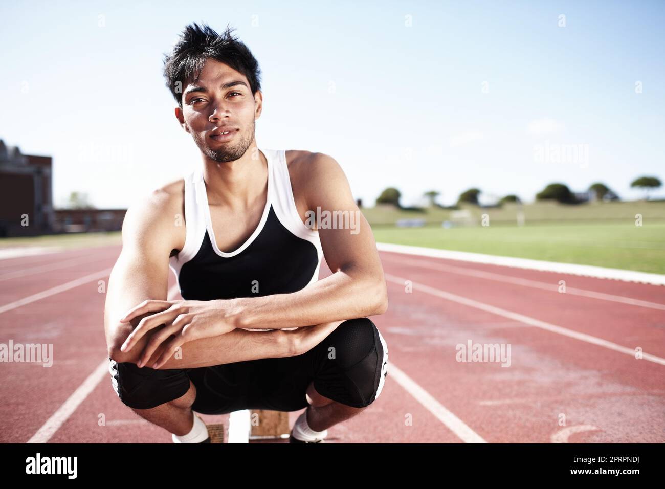 He is highly focussed and determined to win. A young runner crouching on a race track. Stock Photo