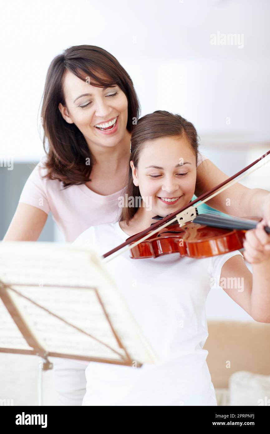 Youre amazing, my girl. A laughing mother helping her smiling daughter practice the violin. Stock Photo