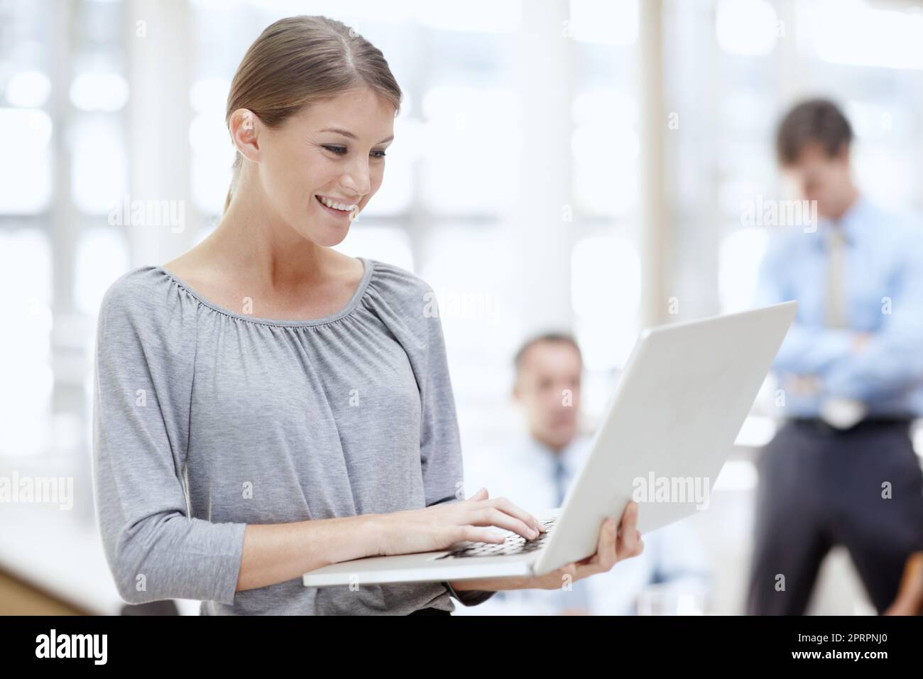 Checking out the new work layout. An attractive young woman using her laptop in the office with her colleagues behind her. Stock Photo