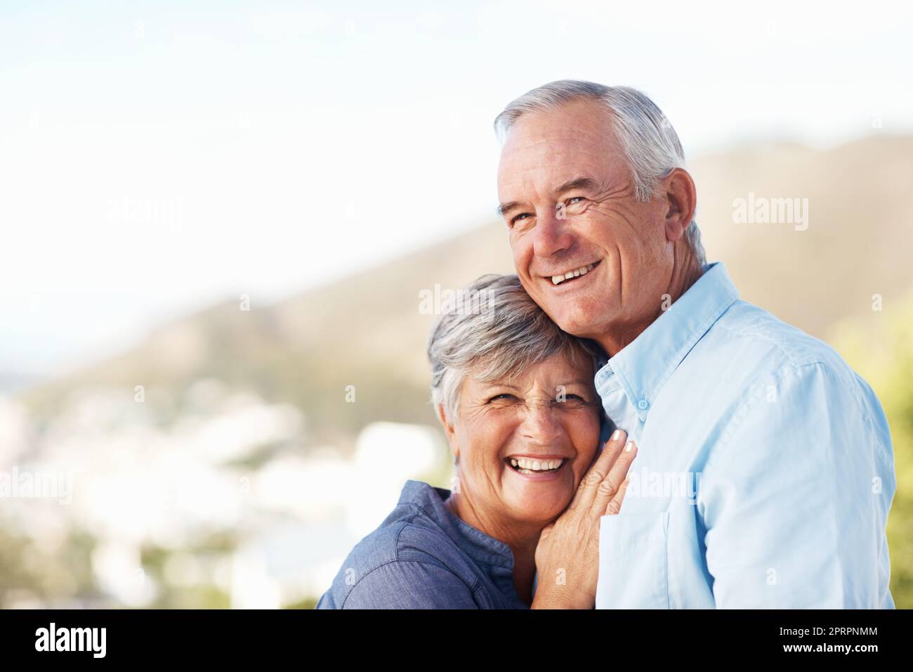 Cute mature couple smiling. Portrait of smiling mature woman leaning on mans chest with mountain in background. Stock Photo