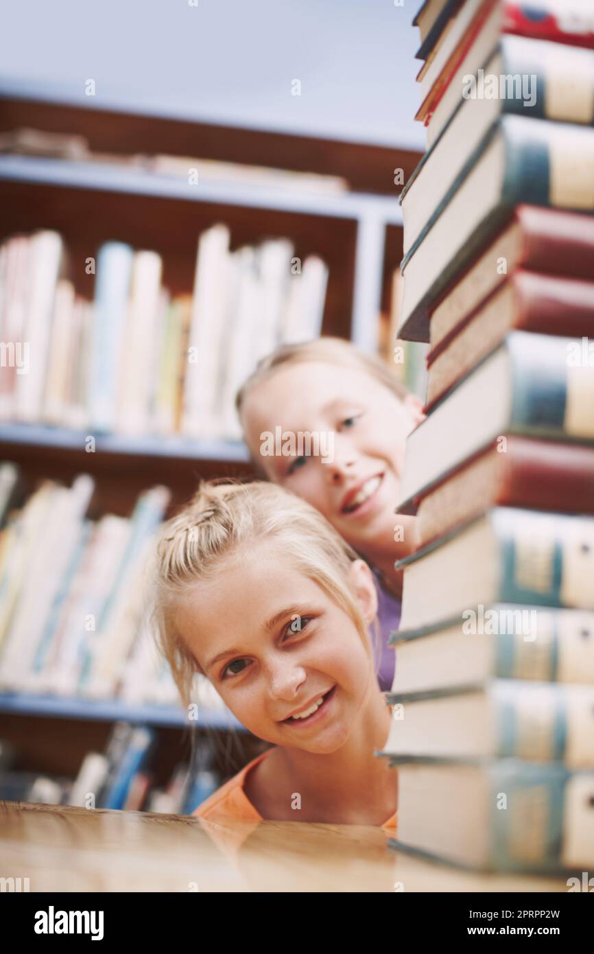 Ive read all of these. Two schoolkids peeking around a stack of books at the library. Stock Photo