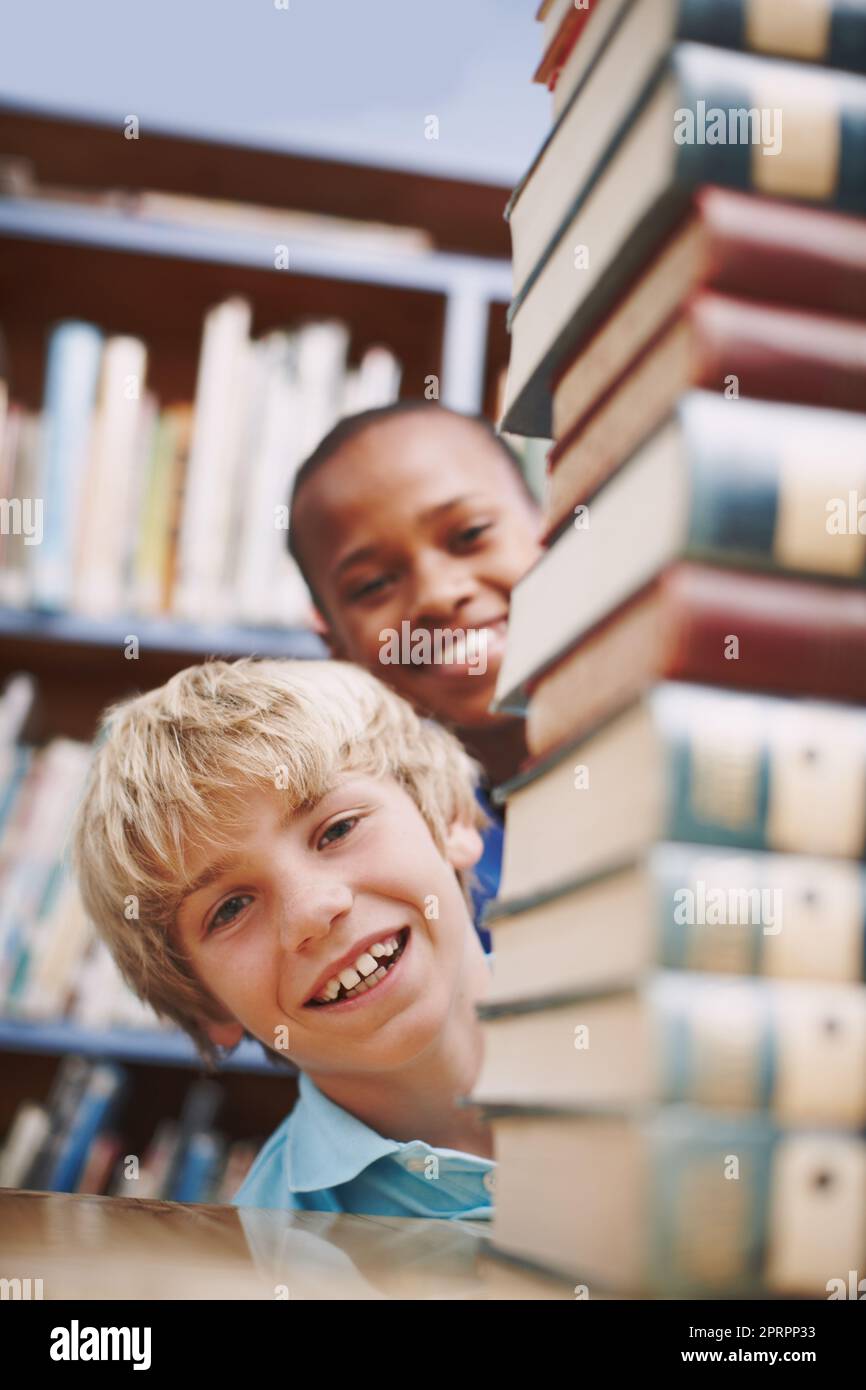 How will we ever get through all of these. Two schoolkids peeking around a stack of books at the library. Stock Photo