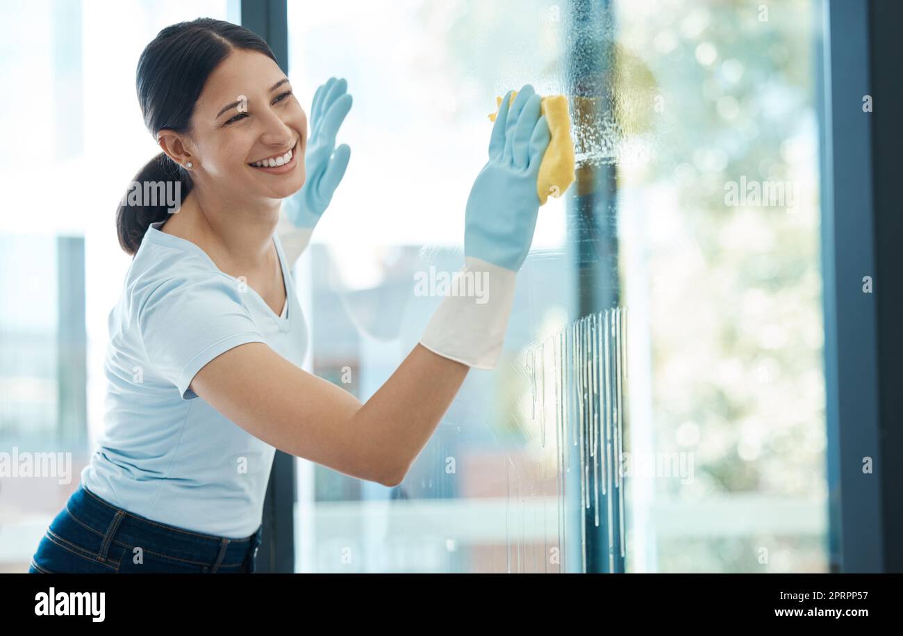 Cleaning, window and service worker woman with glass water product or chemical liquid with a smile for happy job or career. Cleaner working in modern apartment or building and scrub dirt with sponge Stock Photo