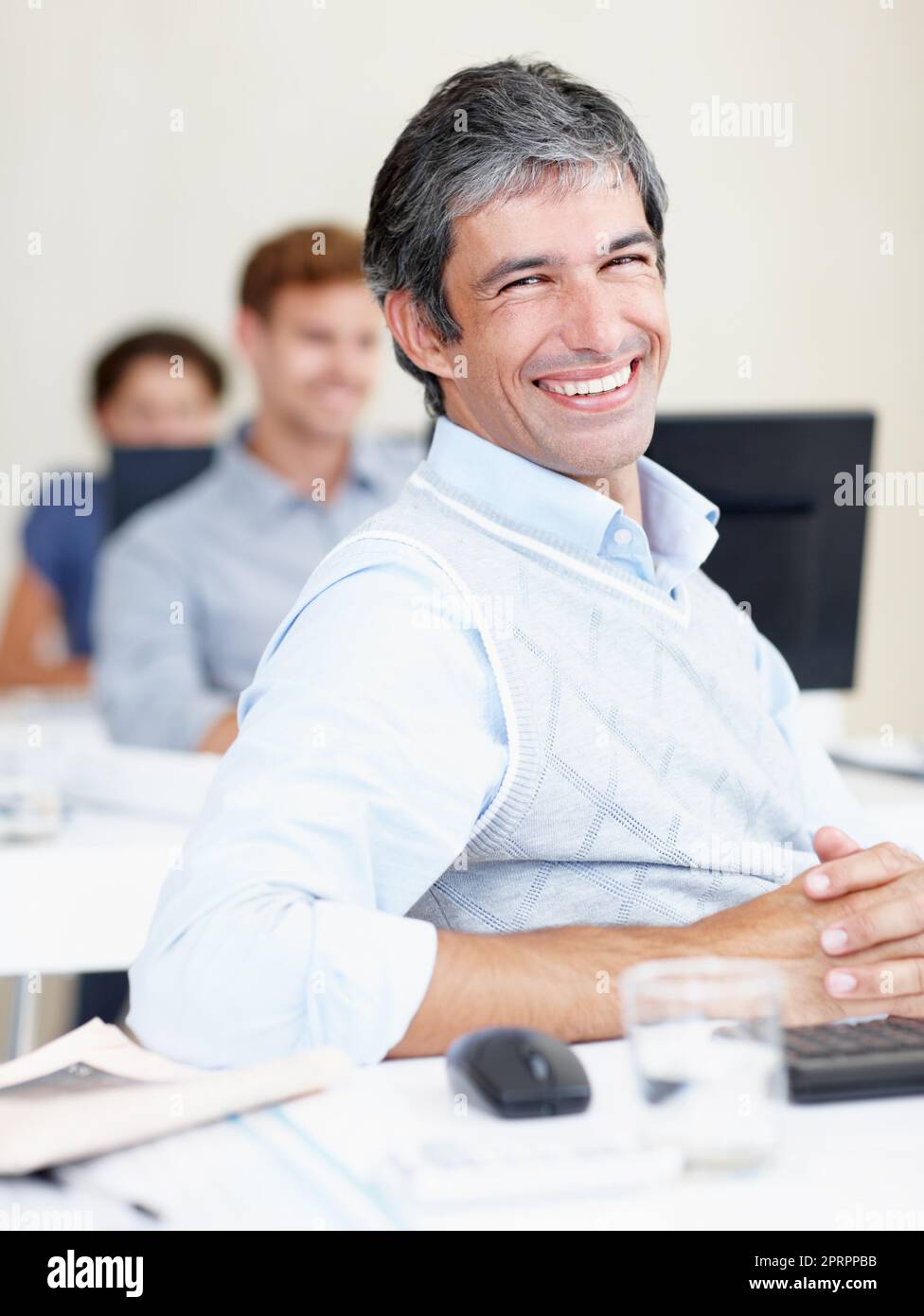 A happy Amazon employee sitting at their desk, surrounded by computers and coworkers