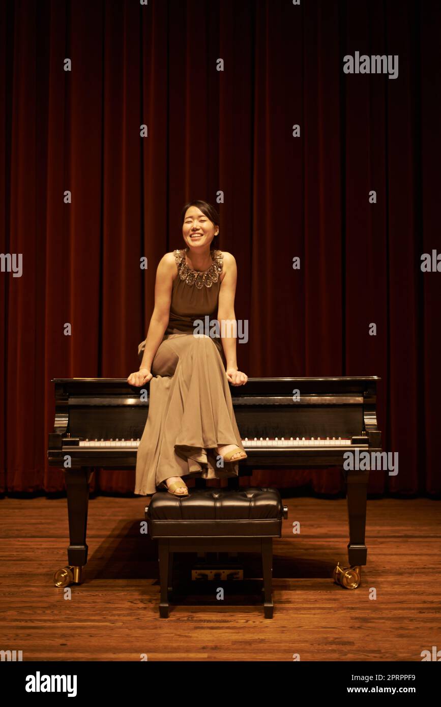 Shes a professional piano player. a young woman sitting on her piano at the end of a musical concert. Stock Photo