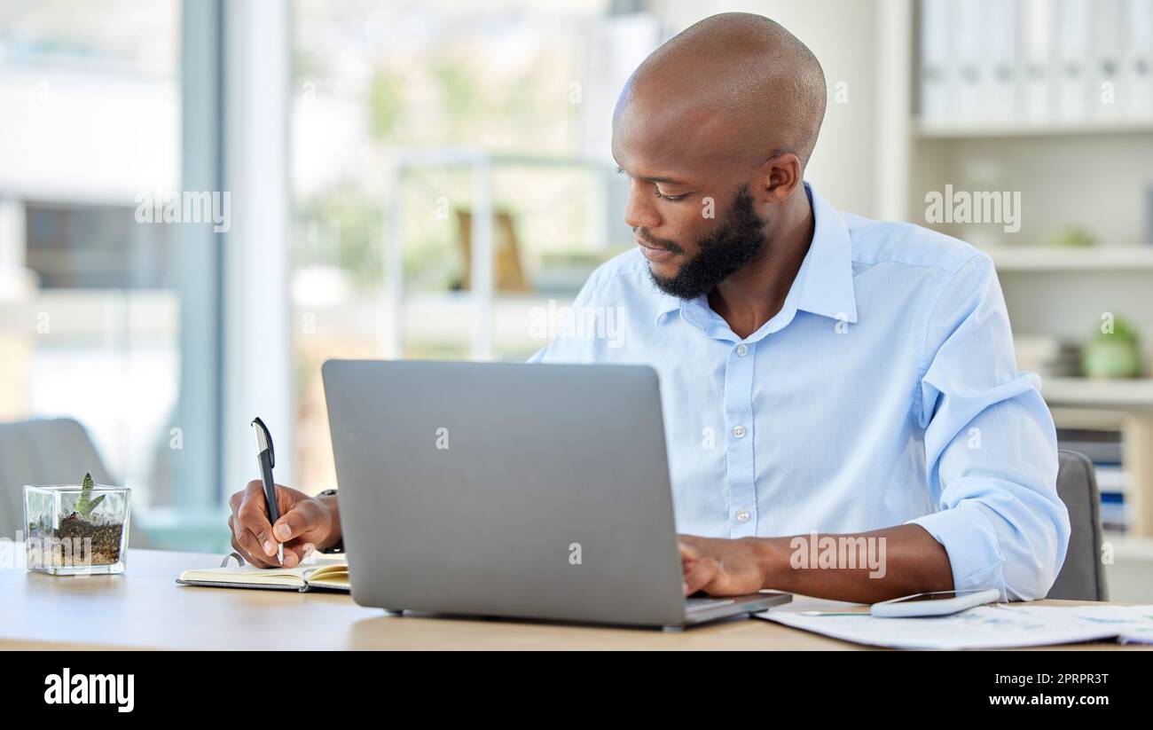 Planning notebook, laptop and businessman working online idea, brainstorming or project management at an office desk. Productive corporate black man writing website ecommerce or tech finance strategy Stock Photo