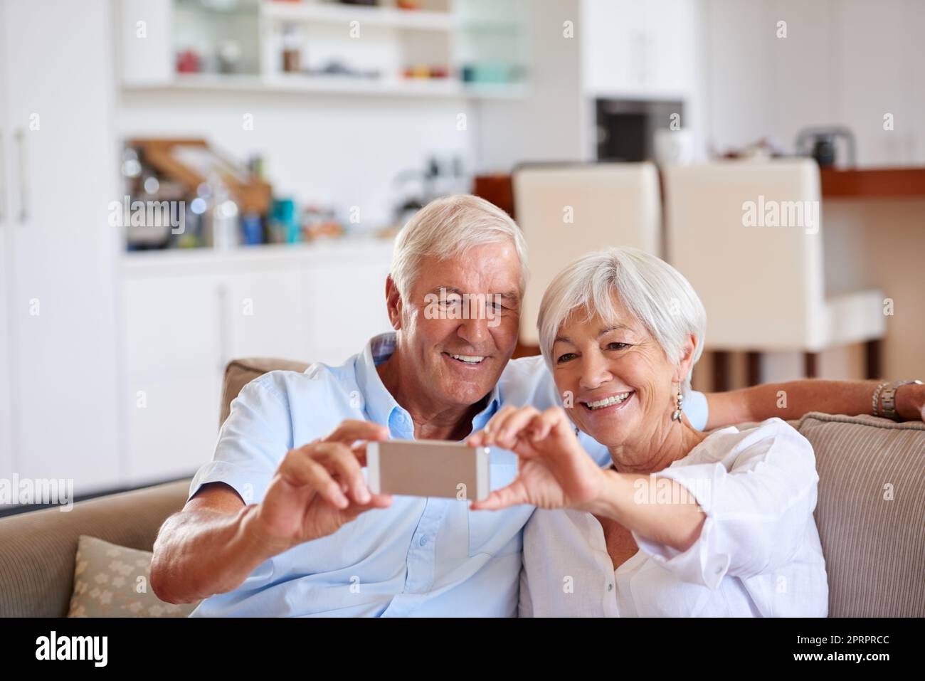 Lets send this one to our children. a senior couple taking a selfie with their cellphone while sitting on the sofa. Stock Photo