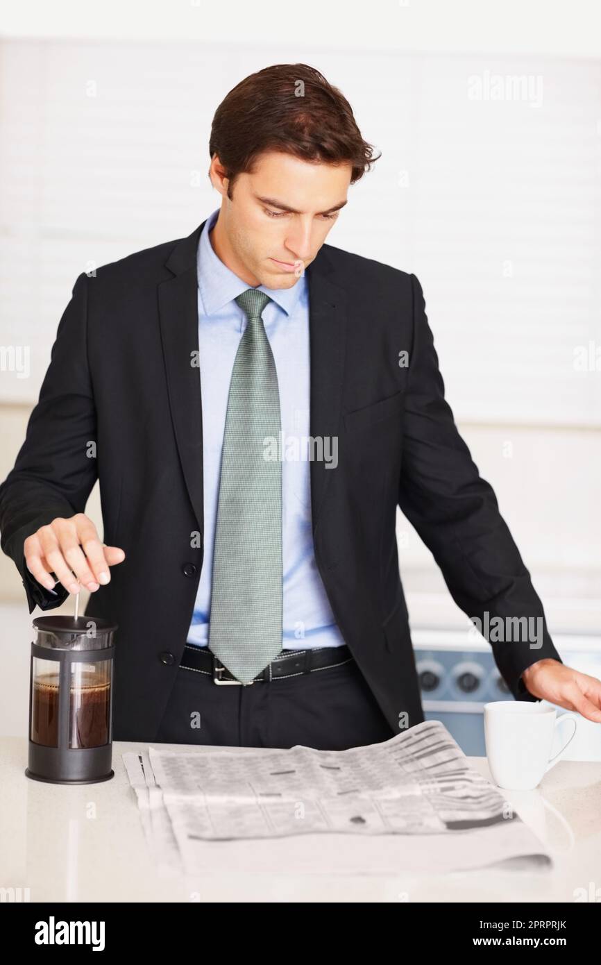 Business man reading newspaper and making coffee in the kitchen. Smart business man reading newspaper while preparing coffee at the kitchen counter. Stock Photo