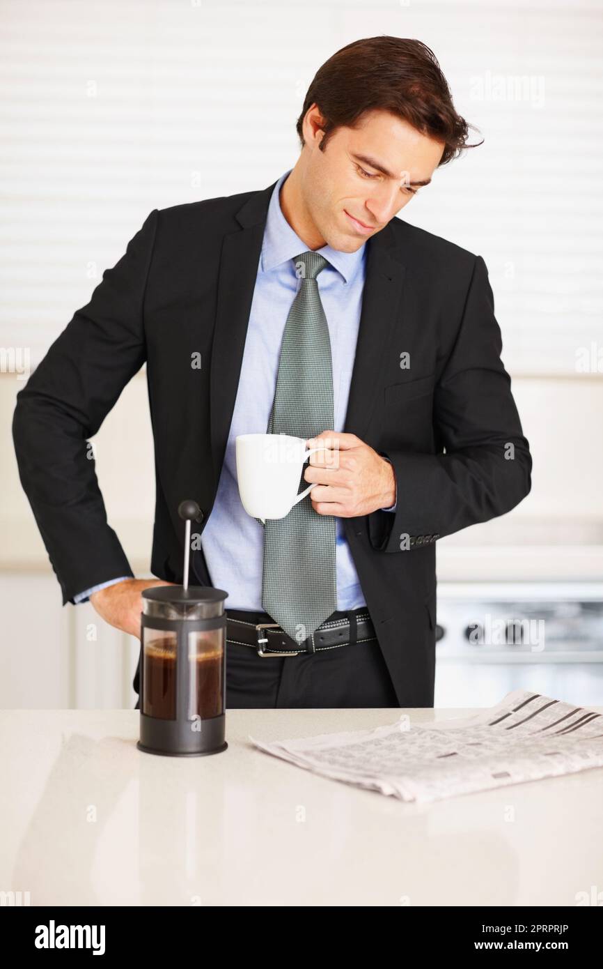 Young man reading newspaper while drinking coffee at home. Business executive reading newspaper while drinking a cup of coffee at home. Stock Photo