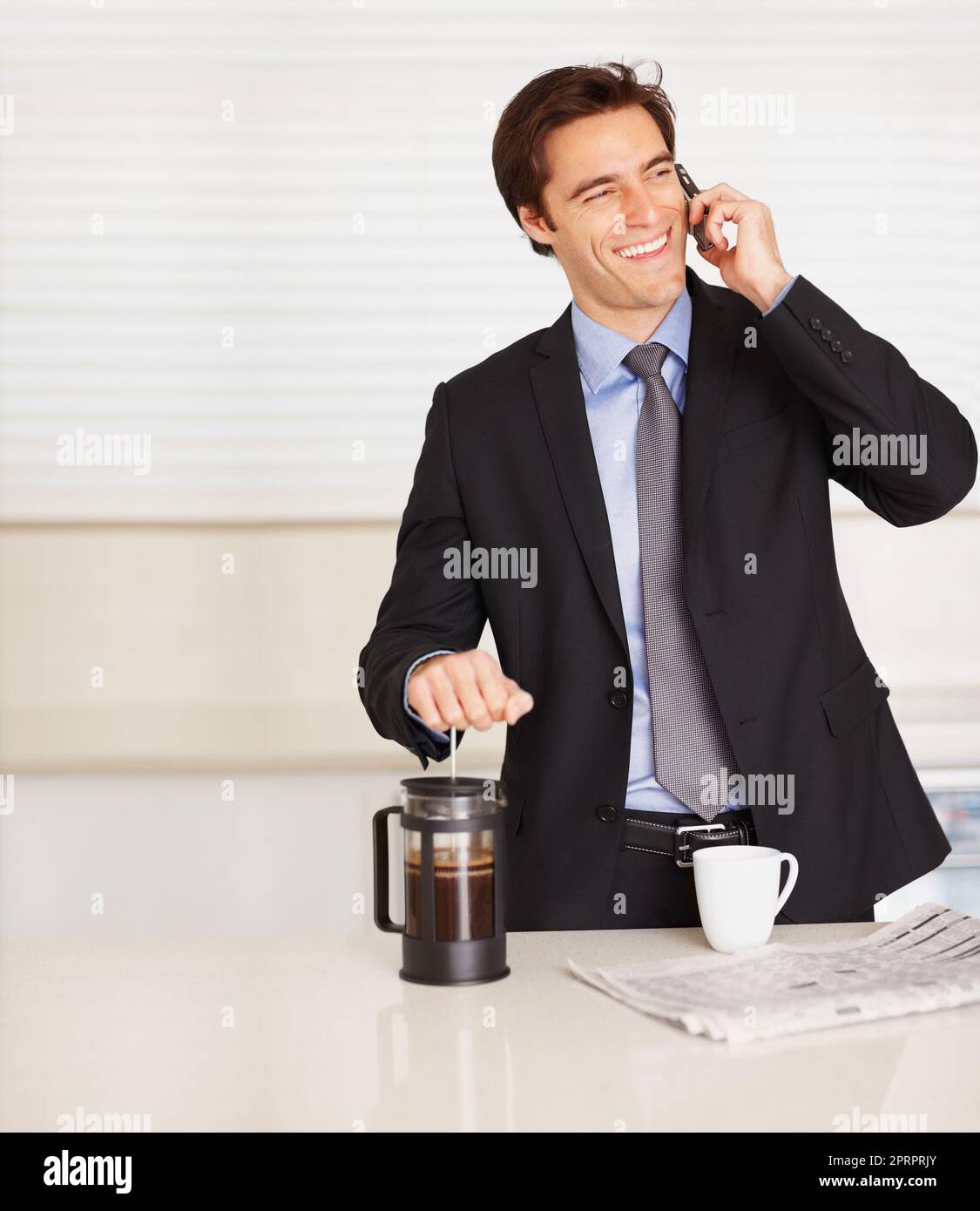 Young business man using cellphone while preparing coffee. Happy business man talking over cellphone while preparing coffee at home. Stock Photo