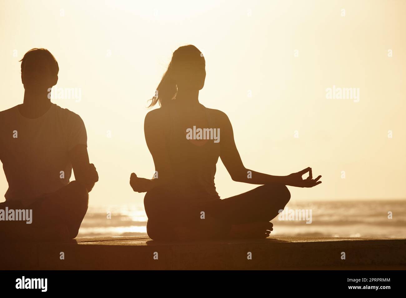 The ideal place for meditation. a couple meditating by the sea at sunset. Stock Photo