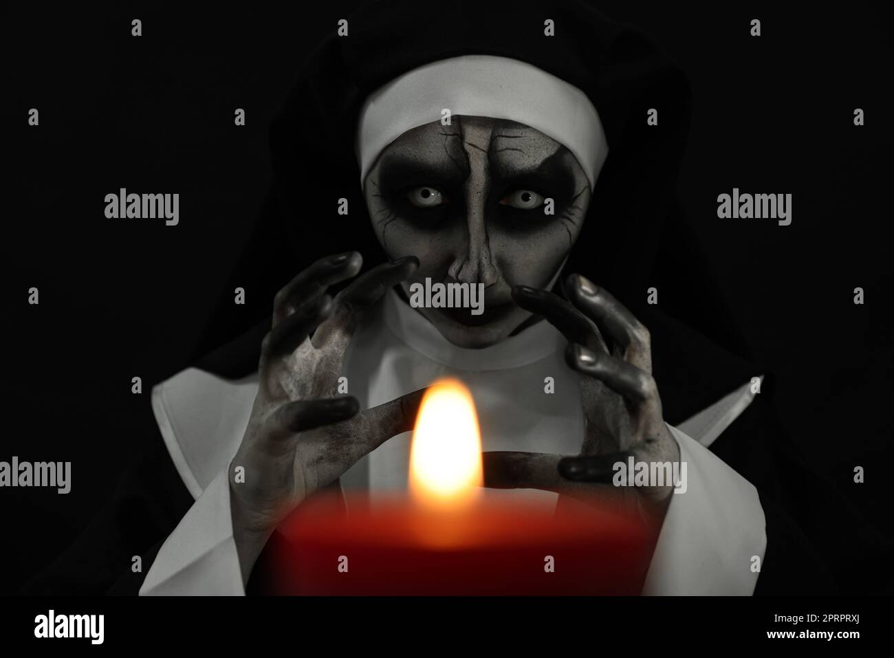 Scary devilish nun with burning candle on black background