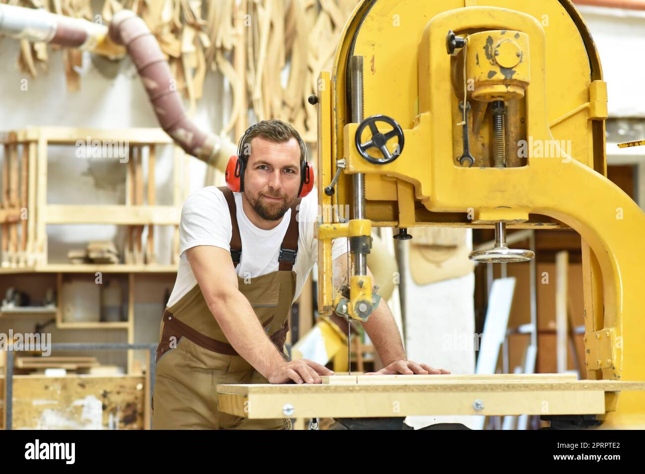 portrait of a carpenter in work clothes and hearing protection in the workshop of a carpenter's shop Stock Photo