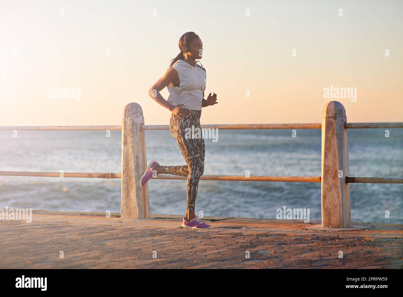 Running with determination. A young woman running along the promenade at sunset. Stock Photo