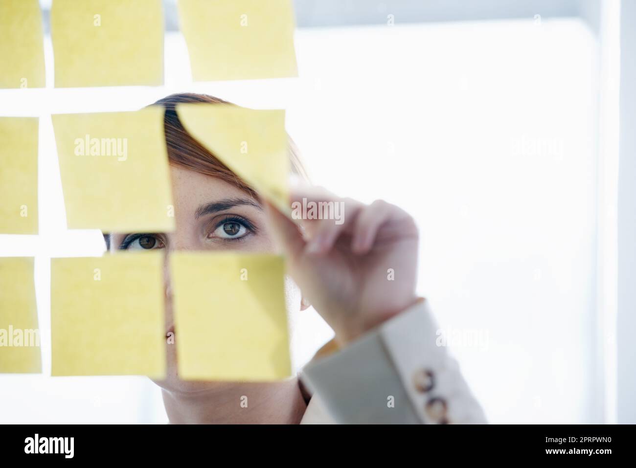 Bringing order to her strategy. a businesswoman arranging sticky notes on a glass wal. Stock Photo