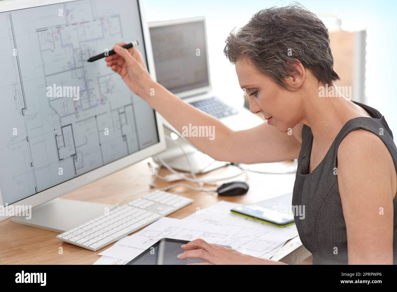 Shes definitely in the right profession. A mature female architect working on building plans on her touchscreen computer. Stock Photo