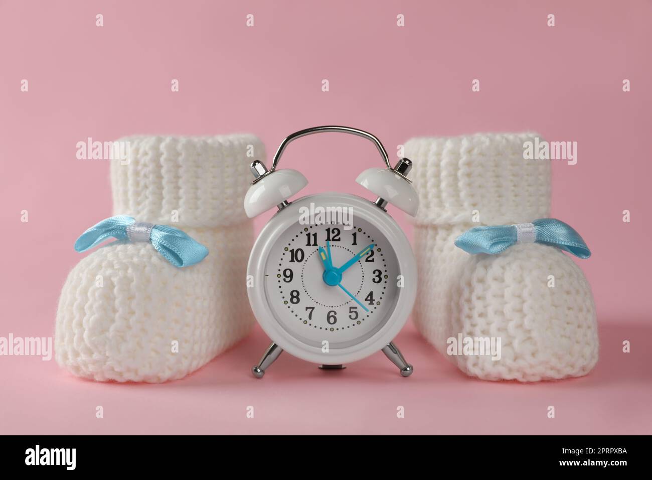 Alarm clock and baby booties on pink background. Time to give birth