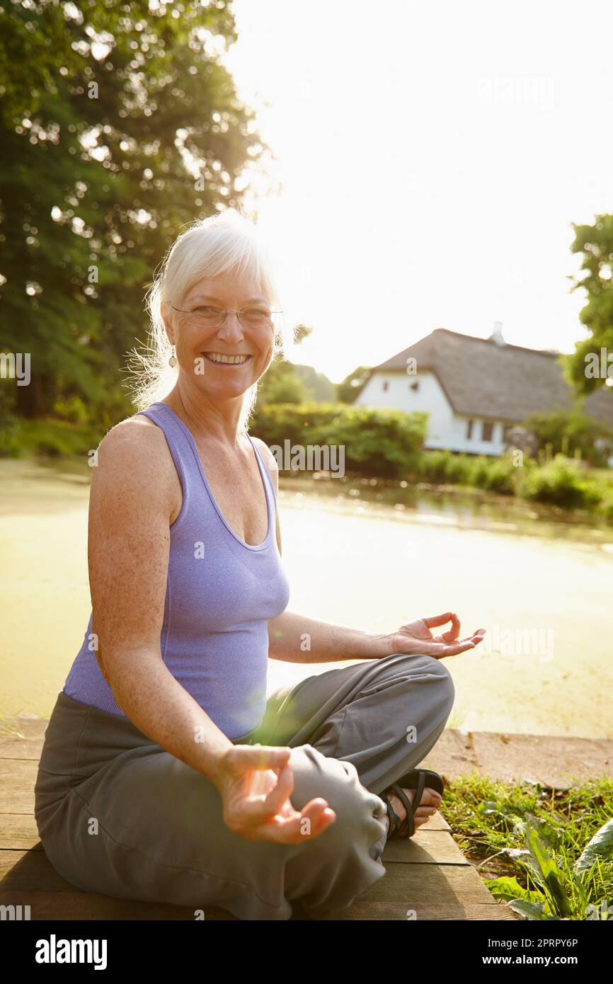 It gives me peace of mind. Portrait of an attractive mature woman sitting in the lotus position in a garden setting. Stock Photo