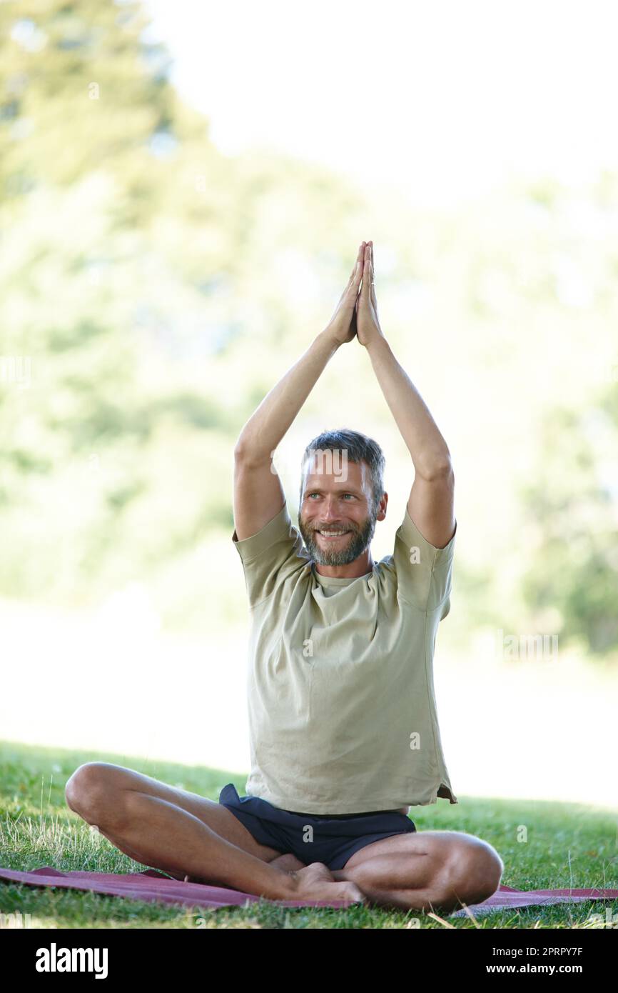 Its his time to unwind. Full length shot of a handsome mature man doing yoga outdoors. Stock Photo