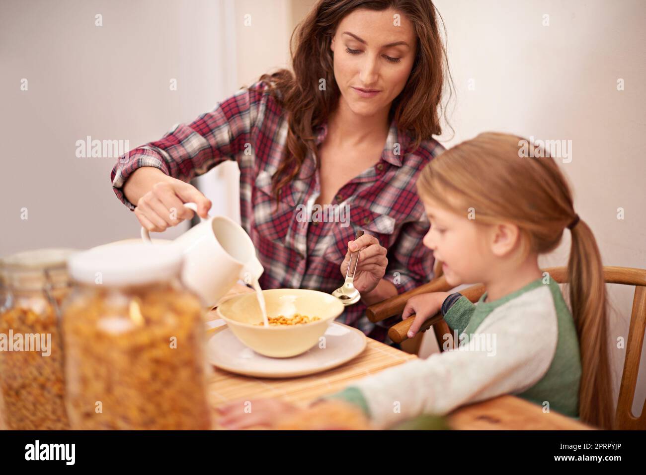 She loves her cereal. a woman pouring milk over her daughters cereal at