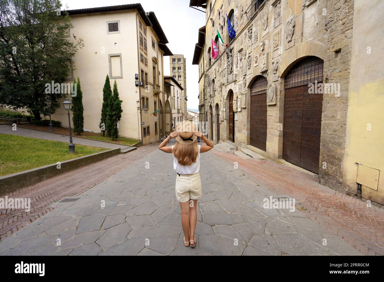 Tourism in Italy. Full length of beautiful tourist girl holding hat enjoys visiting the historic town of Arezzo, Tuscany, Italy. Stock Photo