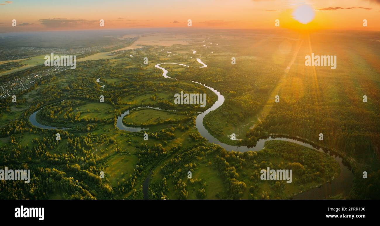 Aerial View. Beautiful Sunset Sun Sunshine Above Green Forest, Meadow And River Landscape In Sunny Evening. Top View Of European Nature From High Attitude In Summer Sunrise. Bird's Eye View. Panorama Stock Photo