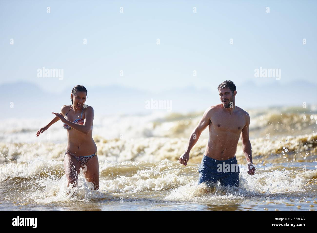 Sharing a summer getaway. a laughing young couple walking out of the surf together. Stock Photo