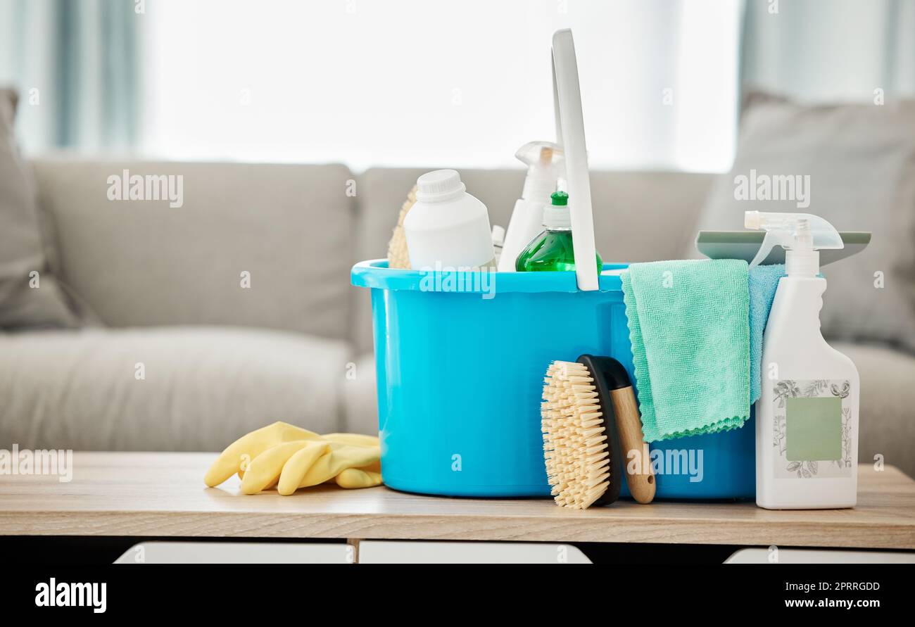House, cleaning service and container with spray bottle, rubber gloves and scrub in home living room or apartment interior. Spring clean day, career or housekeeping with household products on table Stock Photo
