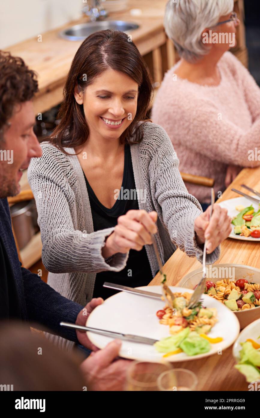 More salad. a family sharing a meal around the dinner table. Stock Photo