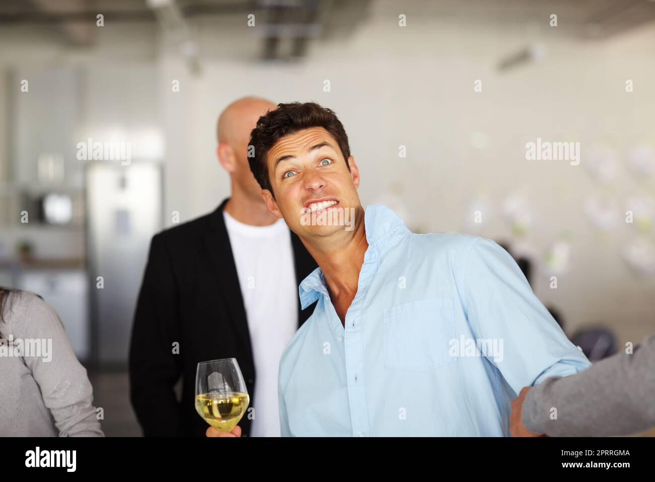 Free booze freakout. A drunk man holding a glass of wine and pulling faces at an office social. Stock Photo