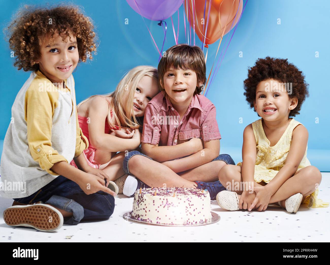 My birthday wish is to be friends forever. a group of children sitting around a birthday cake with bunch of balloons in the background. Stock Photo