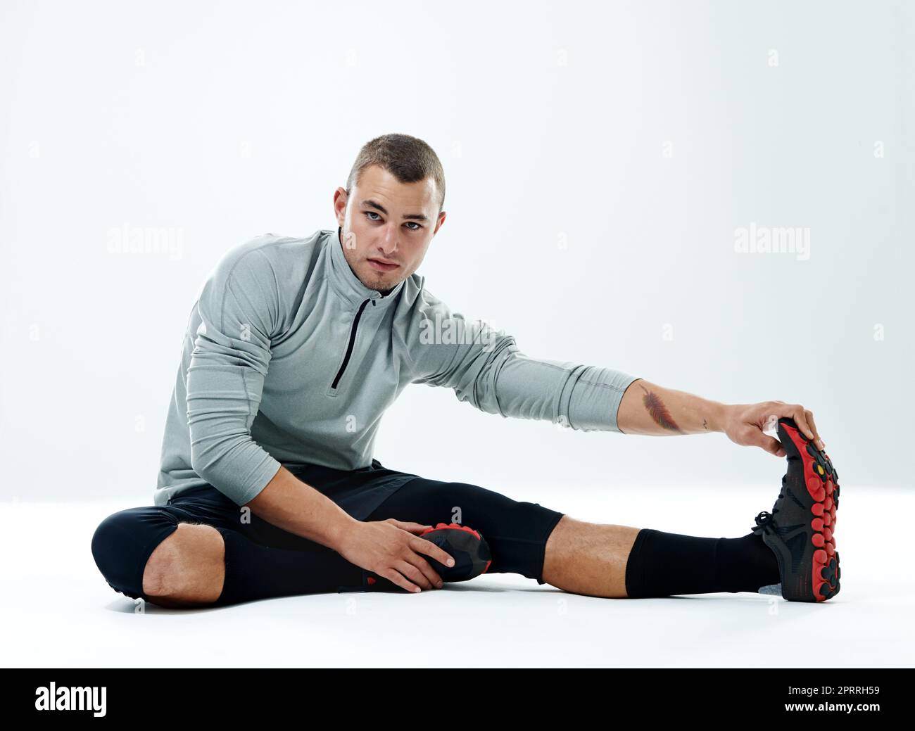 Im one work-out stronger than yesterday. Portrait of a handsome young man sitting in a studio while doing stretches. Stock Photo