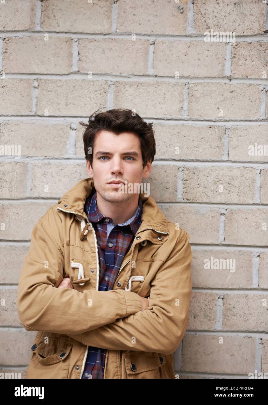 Hes got a red hot attitude to keep him warm. a handsome young man standing against a brick wall with his arms crossed. Stock Photo