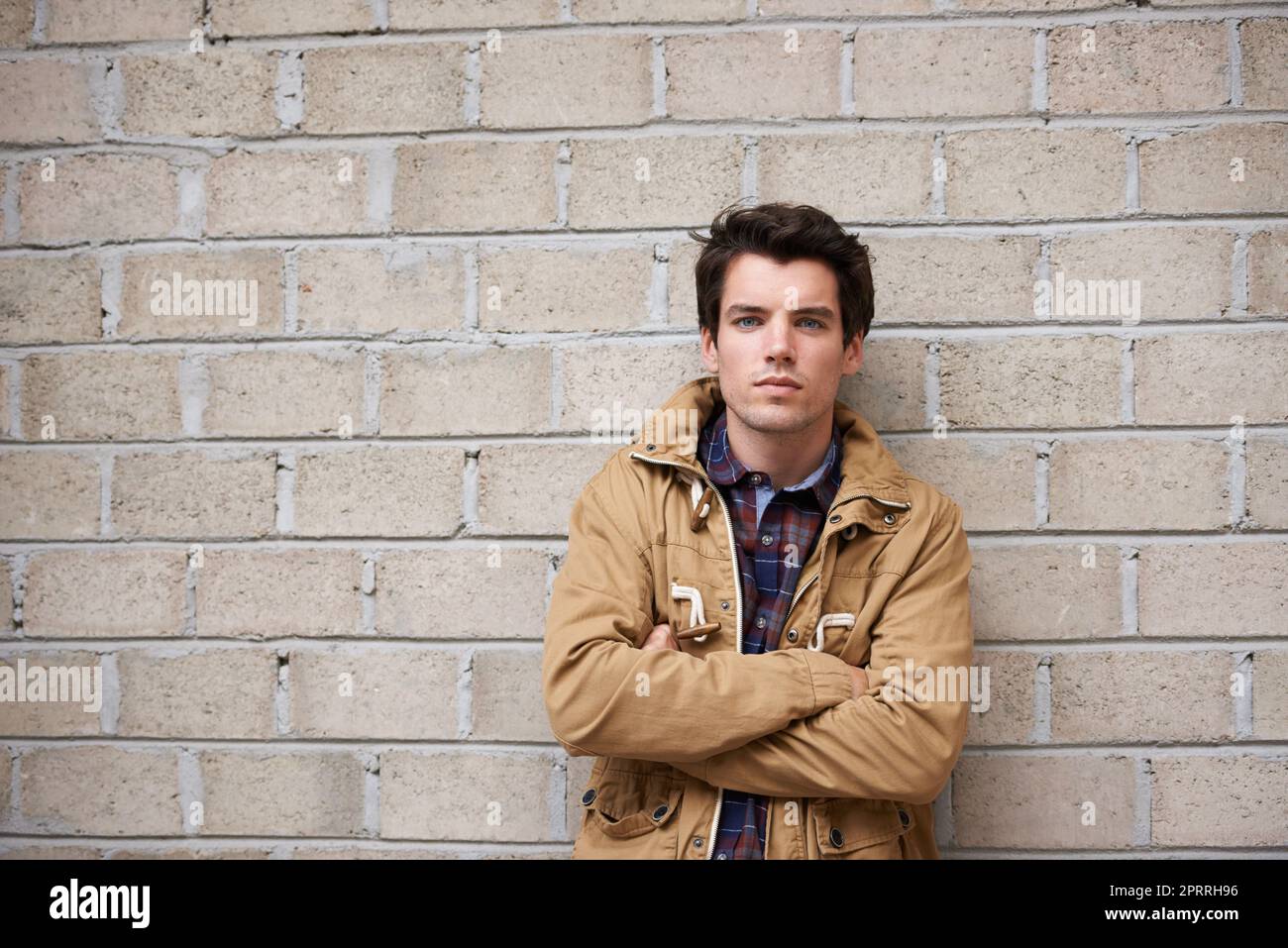 a young man leaning against a brick wall with his arms crossed Stock Photo