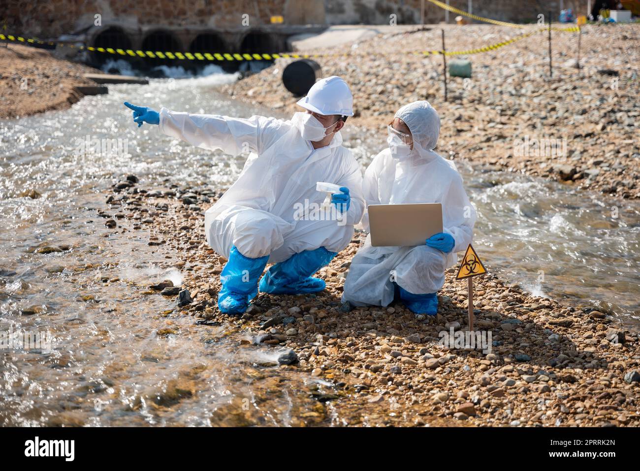 Biologist wear protective suit and mask collects sample of waste water from industry Stock Photo