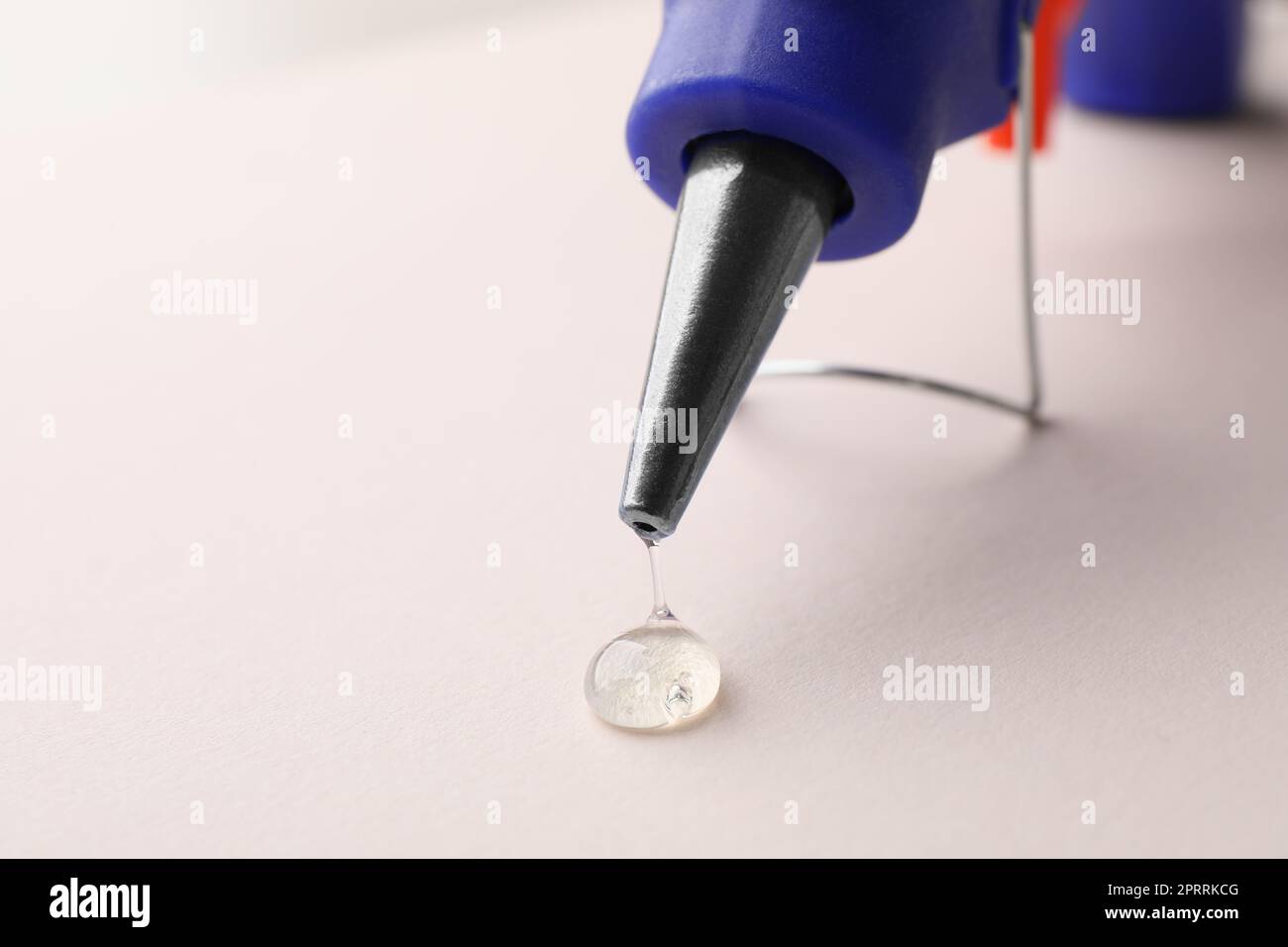 Melted glue dripping from hot gun on white table, closeup. Space for