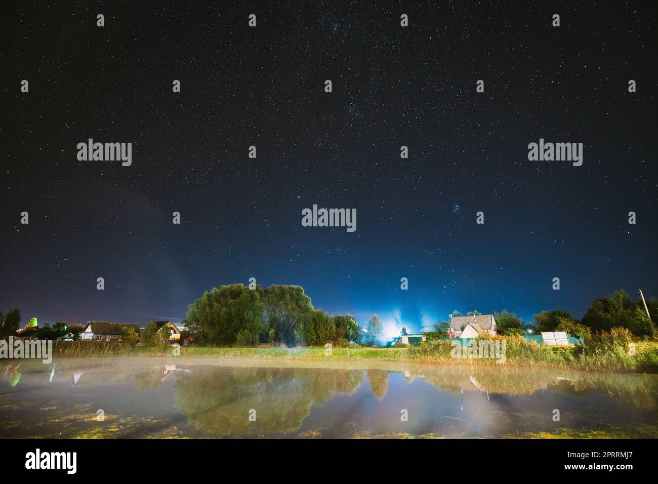 Evaporation Over River Lake Near Houses In Village. Milky Way Galaxy In