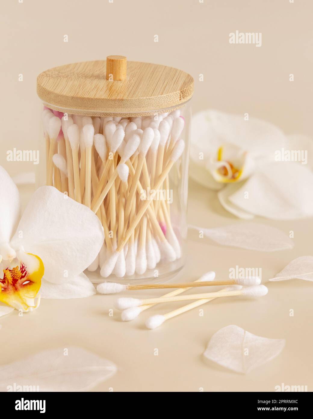 Bamboo cotton buds in a jar near white orchid flowers on light beige. Eco friendly skincare
