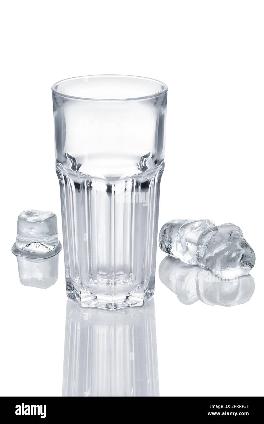 Empty faceted glass and three ice cubes melting on white glass table Stock Photo