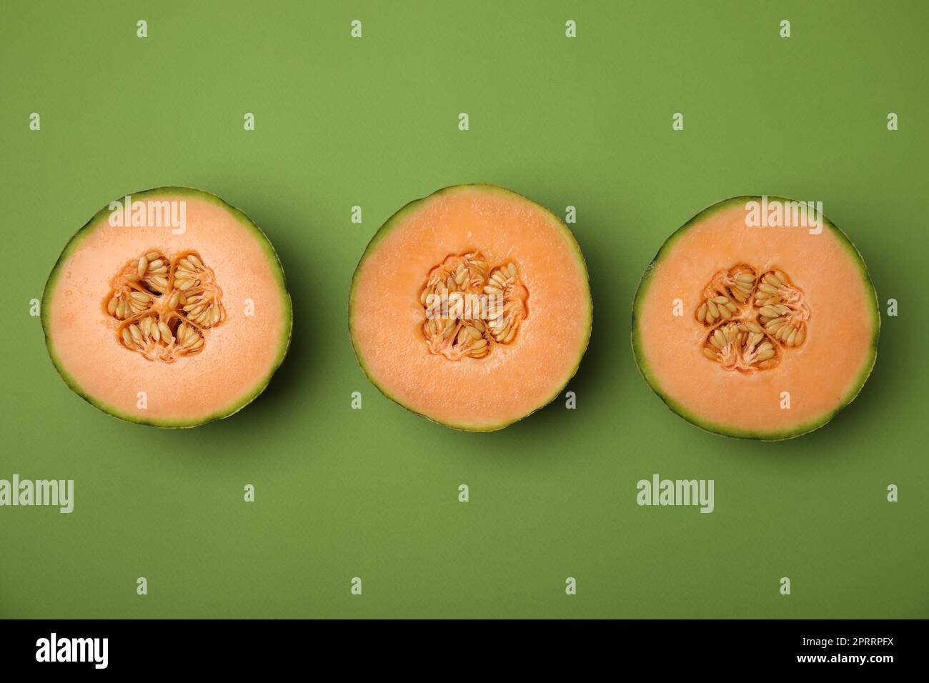 Cut melons on green background, flat lay Stock Photo
