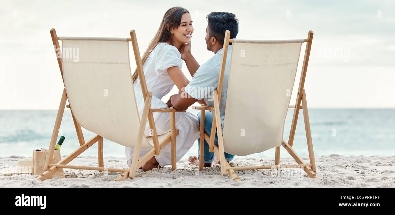 Happy, travel and love of a couple from India on a beach, ocean and sea vacation. Happiness of Indian people smile with a peace, relax and calm mindset together by the waves, sand and water in nature Stock Photo