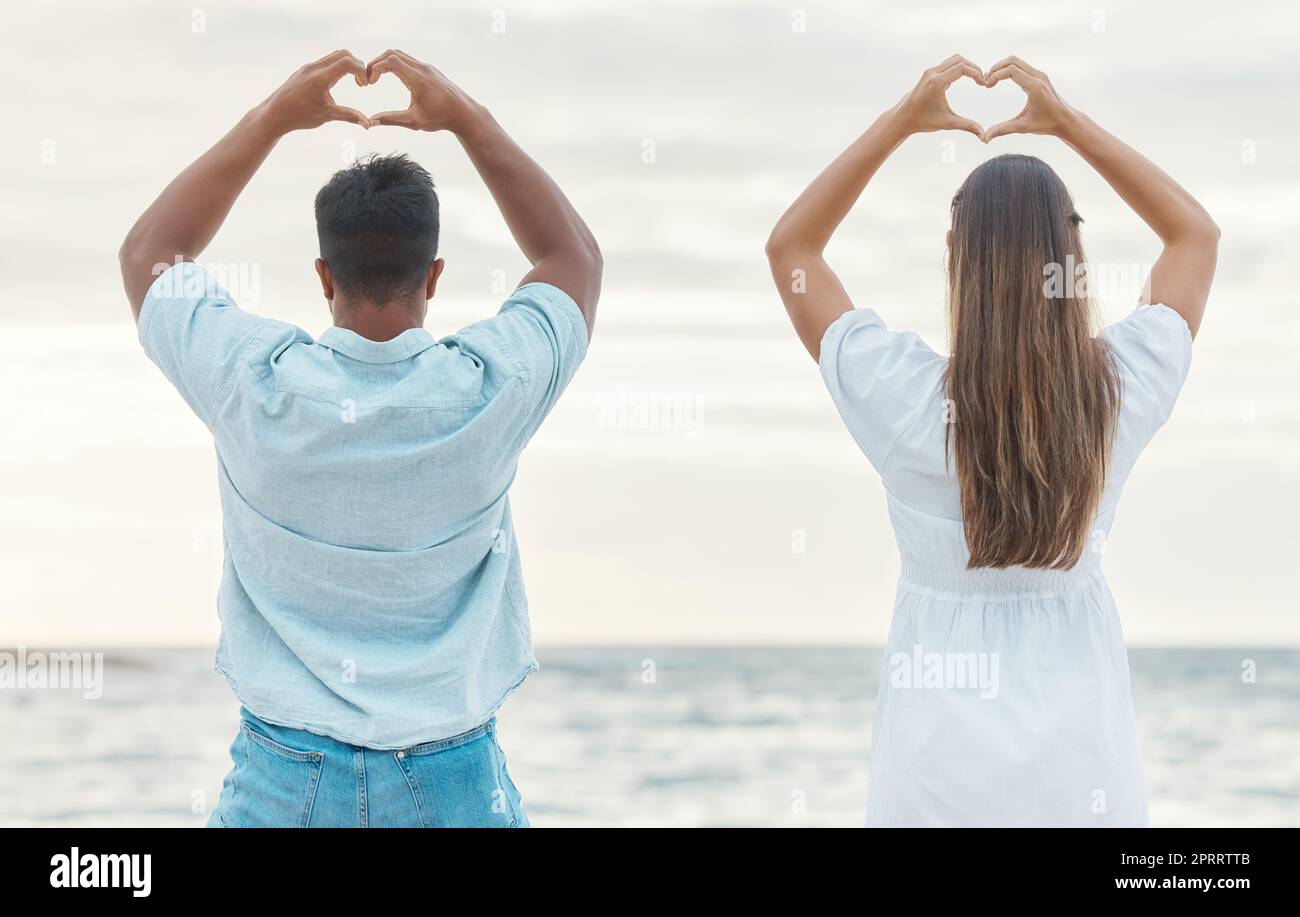 Couple hands, back heart love sign and passion, affection or romantic emoji by the ocean. Romance, man and woman, hand symbol or emotion shape. Intimacy or adoration, support or devotion gesture. Stock Photo
