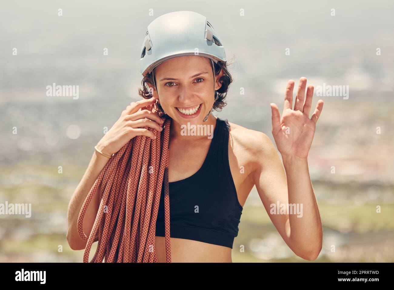 Rock climbing, rope and woman portrait happy to challenge her fitness and hiking outdoors in nature adventure. Helmet, smile and mountain climber girl waving and ready for exercise and sports workout Stock Photo