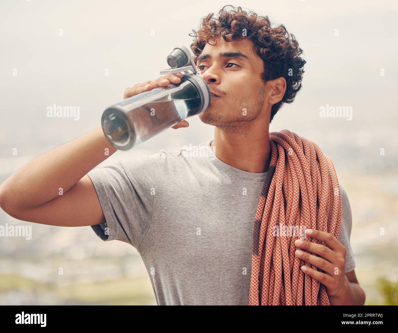 Sports man drinking water, hiking or rope rock mountain climbing adventure, workout or exercise outdoor. Wellness fitness and extreme sport climber with health, relax and refreshing liquid on break. Stock Photo